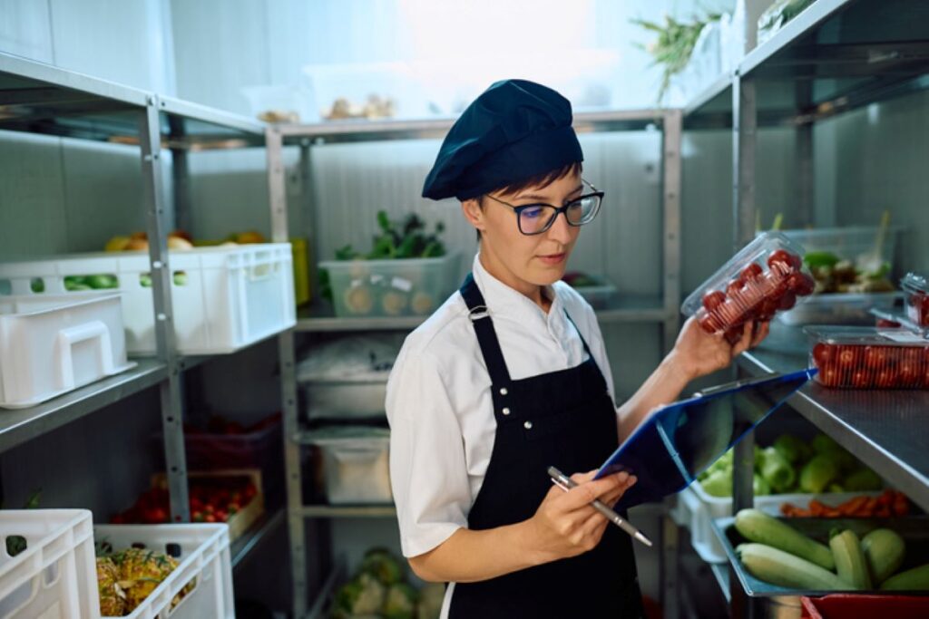 A chef in glasses takes stock of her ingredients in a walk-in fridge